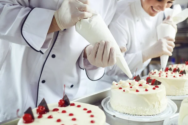 Dos pasteleros decoran un pastel de una bolsa en una pastelería — Foto de Stock