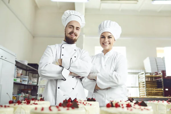 Los pasteleros en uniforme blanco sonríen en la panadería . — Foto de Stock