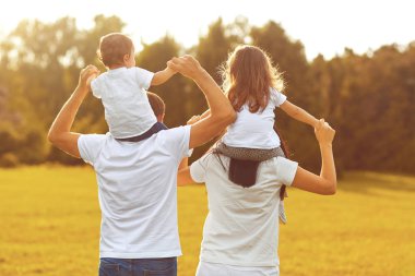 Arkadan görüntüleyin. Çocuklu bir aile bir parkta çim üzerinde yürüme .