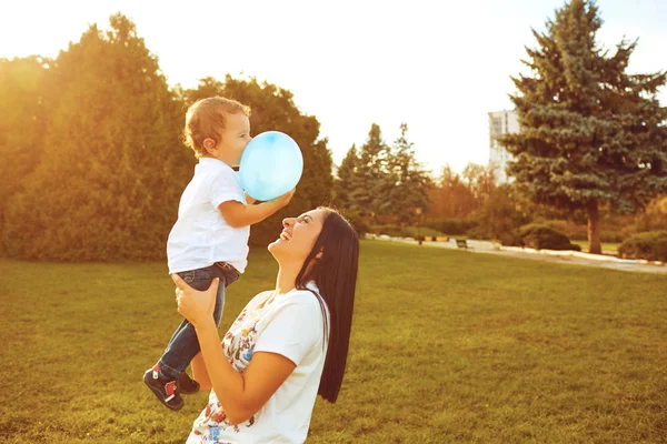 Matka z małym chłopcem w ramionach uśmiecha się w letnim parku. — Zdjęcie stockowe