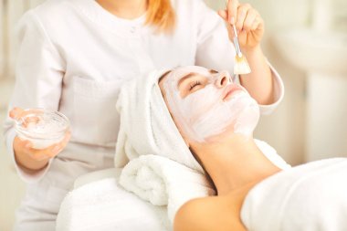 Güzellik spa salonunda bir kadın için beyaz bir maske uygular.