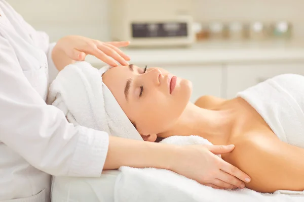 Masaje facial para una joven tumbada en un salón de belleza . — Foto de Stock