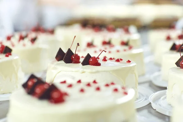 La guinda roja sobre la torta blanca sobre la mesa con los pasteles —  Fotos de Stock