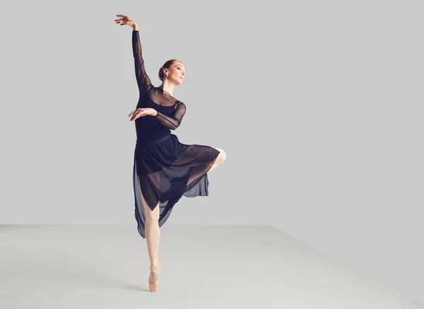 Ballerina w czarnym Tutu elegancko tańczy na czarnym tle. — Zdjęcie stockowe