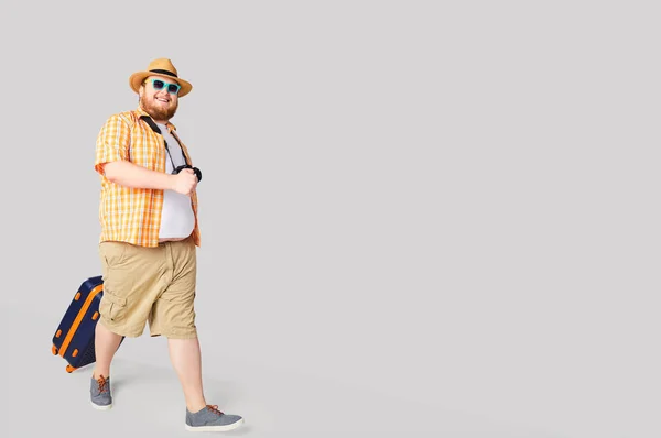 Fat funny man with a suitcase smiling on a gray background.
