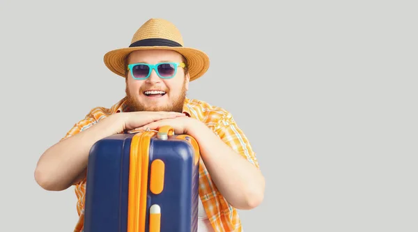 Смішний товстун у капелюсі з валізою посміхається на сірому фоні . — стокове фото