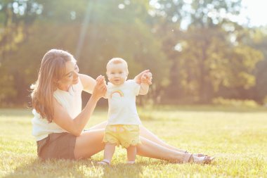 Çimenlerin üzerinde günbatımında oynayan çocuk ile anne.