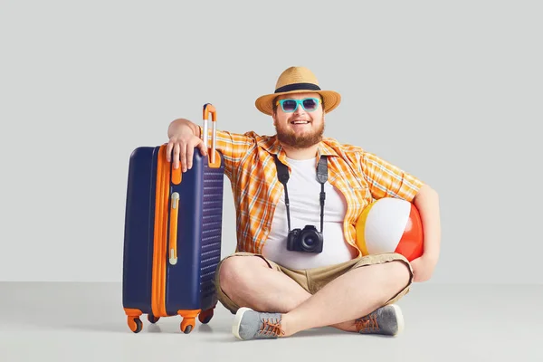 Gruby zabawny człowiek z walizka uśmiechnięta na szarym tle. — Zdjęcie stockowe