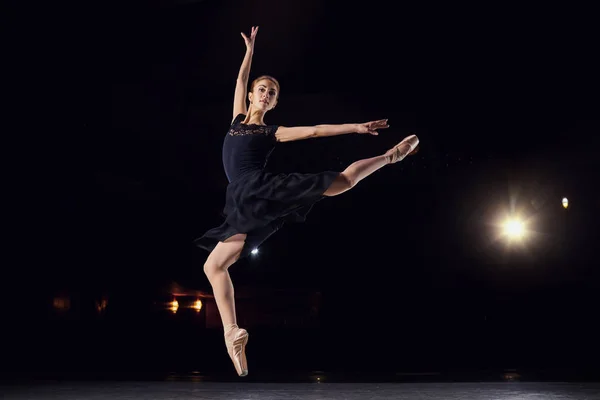 Балерина в чорному костюмі стрибає на чорному фоні. — стокове фото