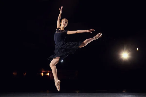 Bailarina em um terno preto está pulando em um fundo preto . — Fotografia de Stock