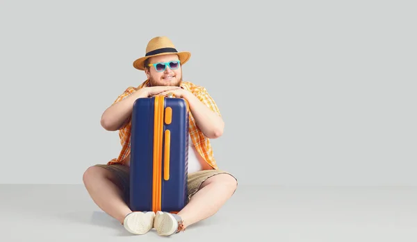 Товстий смішний чоловік з валізою посміхається на сірому фоні . — стокове фото