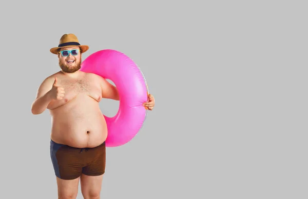 Dikke grappige man in zwembroeken met een opblaasbare ring op een grijze achtergrond. — Stockfoto