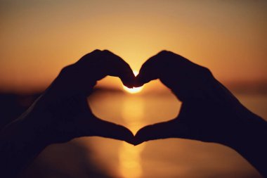 Deniz günbatımı üzerinde kalp şeklinde el.