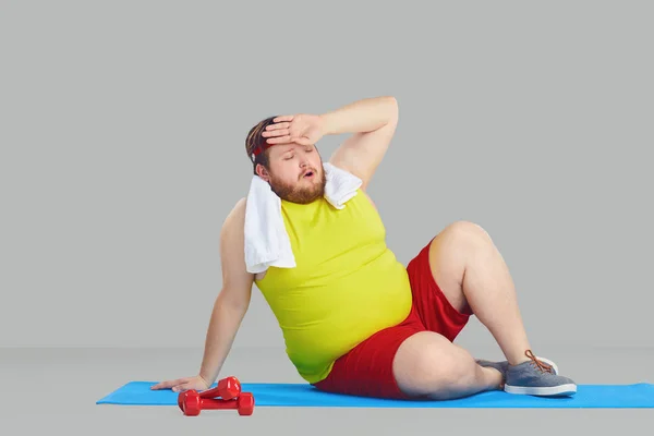 Un hombre gordo en ropa deportiva cansado de un fondo gris . — Foto de Stock