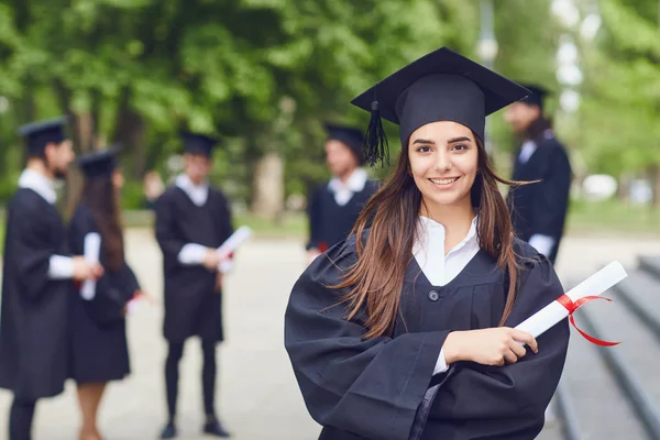 Üniversite mezunlarının arka planına karşı genç bir kadın mezun. — Stok fotoğraf
