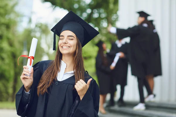 Egy fiatal női diplomás, a görgetés háttérrel egyetemi diplomások. — Stock Fotó