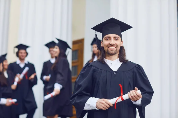 Männliche Hochschulabsolventen lächeln vor dem Hintergrund von Universitätsabsolventen. — Stockfoto
