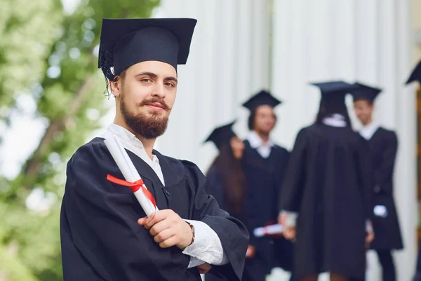 Egy fiatal férfi diplomás a háttérben az egyetemi diplomások. — Stock Fotó