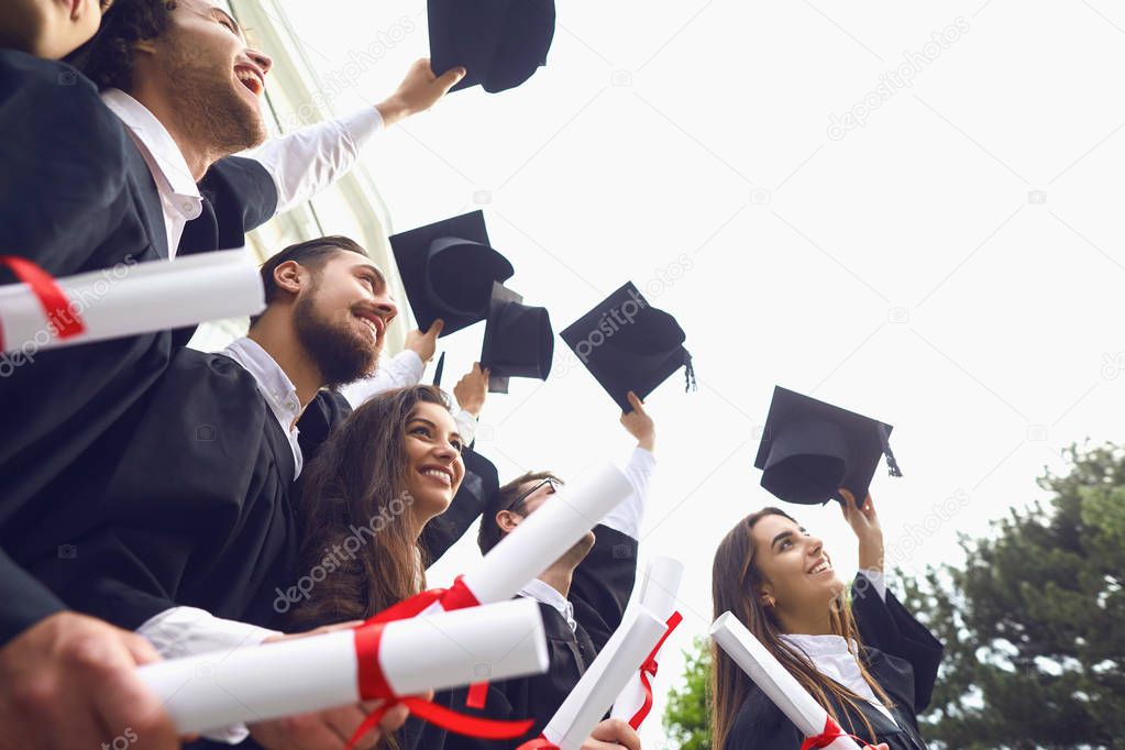 Happy graduates raised their hands with scrolls of diplomas