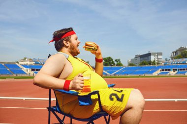 Şişman adam stadyumda eğitim bir burger ve bira yeme.