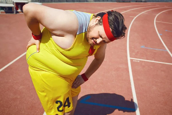 A fat man holds his back in the stadium.