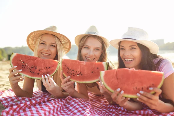 Girlfriends at a party eating a watermelon on the beach.