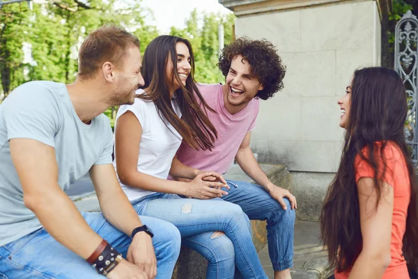 Un grupo de amigos se ríen sentados en un parque . — Foto de Stock