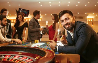 Bir kumarhanede poker oynayan masa ruleti başında oturan bir bardak viskiyle takım elbiseli bir adam..