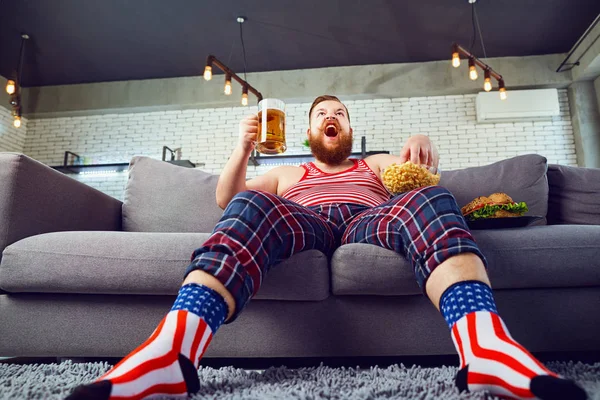 ソファに座ってハンバーガーを食べて厚い変な男. — ストック写真