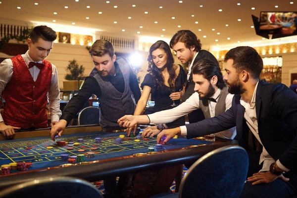 Amigos ricos fazem apostas apostando na mesa de roleta no cassino . — Fotografia de Stock