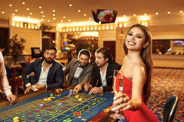 Eine Frau mit einem Glas Champagner in einem Kleid beim Tischroulette im Casino. — Stockfoto