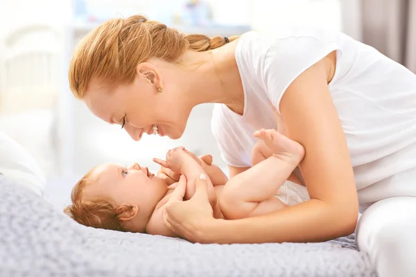 Feliz madre sonríe al bebé acostado en la cama en la habitación . — Foto de Stock