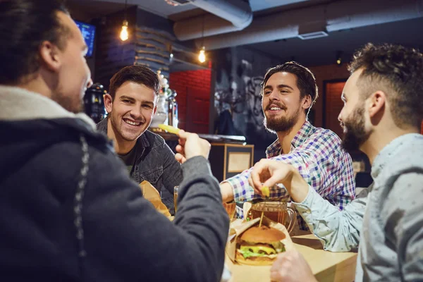 Gelukkig vrienden hamburgers eten, biertje drinken in een bar. — Stockfoto
