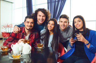 Arkadaşlar bir kafede bir masada oturan kameraya bakıyorlar.