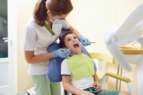 Dentista trata um dente de criança para um menino em um consultório odontológico — Fotografia de Stock