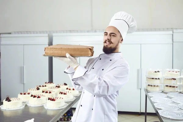 Confeiteiro homem segurando bolo sorrindo em uma pastelaria — Fotografia de Stock