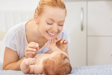 Gülümseyen anne yatakta yatan bebeğine bakıyor