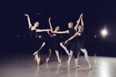 Bir grup balerin siyah bir arka plan aleyhine sahnede dans ediyorlar..