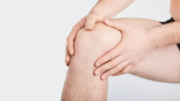 Een man in ondergoed houdt zijn knie met een hand op een grijze achtergrond. — Stockfoto