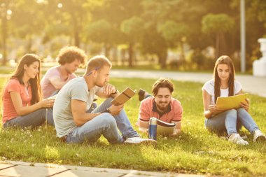 Bir şehir parkında oturan kitap okuyan bir grup öğrenci.