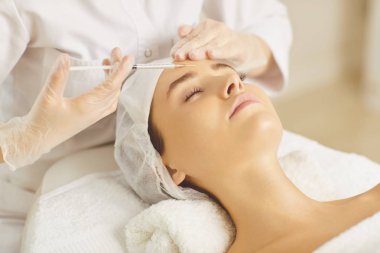 Kozmetoloji doktoru bir kadına güzellik enjeksiyonson yüz yapar.