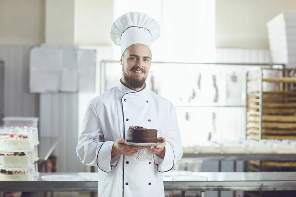 Pastelero hombre sosteniendo pastel sonriendo en una pastelería — Foto de Stock