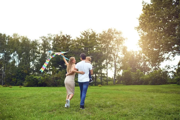 Gelukkige familie loopt met een vlieger door het gras in park. — Stockfoto