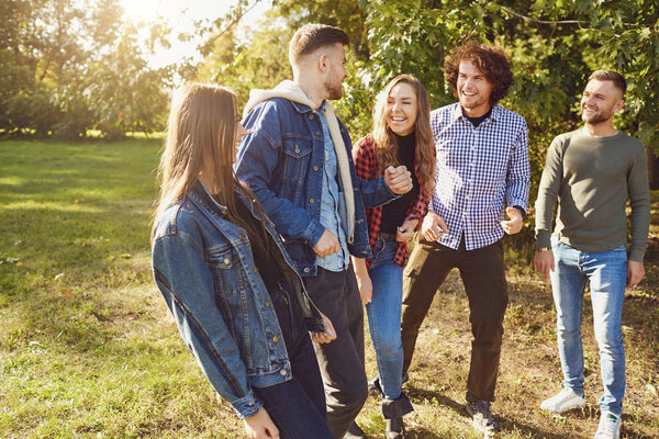 Young people laugh while standing in a park in spring.