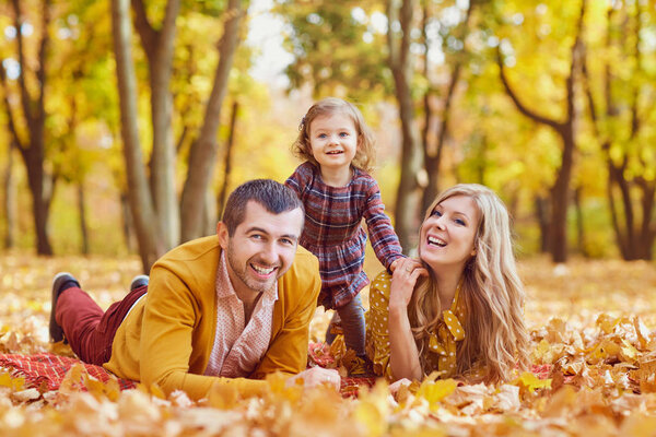 Family lying on yellow leaves in the park in autumn.