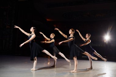 Bir grup balerin siyah bir arka plan aleyhine sahnede dans ediyorlar..