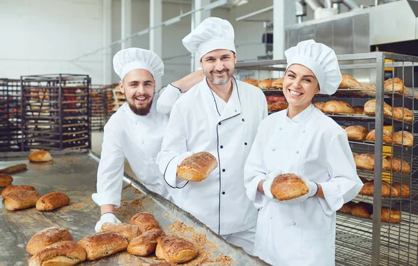 Panettieri sorridenti che tengono il pane fresco tra le mani in un panificio — Foto Stock