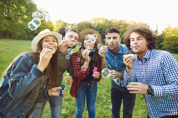 Mladí přátelé foukající v parku mýdlové bubliny — Stock fotografie