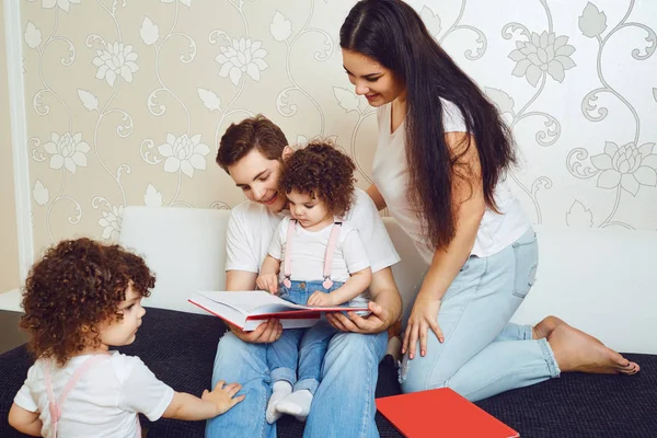 Mãe e pai com filhos lêem um livro enquanto se sentam em um sofá — Fotografia de Stock