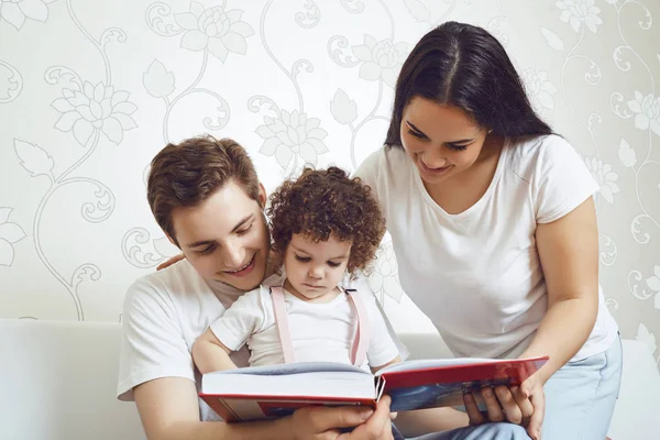 Mãe e pai com filhos lêem um livro enquanto se sentam em um sofá — Fotografia de Stock